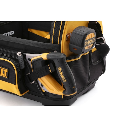 Close-up of a DEWALT tool bag featuring a staple gun and a tape measure attached to the bag. The bag is black and yellow with multiple compartments and durable construction.