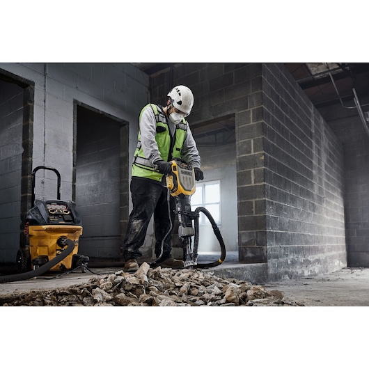 Worker using DEWALT breaker D25966-XE, D25966-B2 on rubble indoors. Construction safety gear worn.