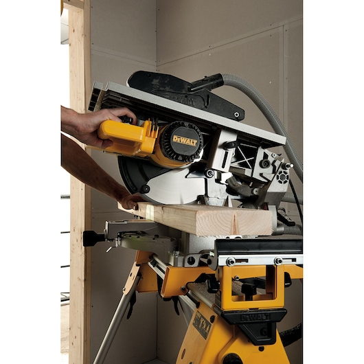 A person operating a DEWALT miter saw to cut a piece of wood inside a workshop.