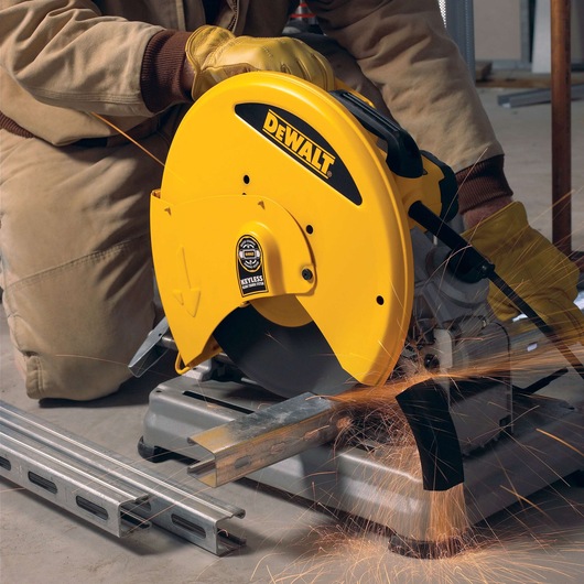 A person wearing protective gloves operates a yellow DEWALT metal cutting saw, producing sparks while cutting a steel beam indoors.
