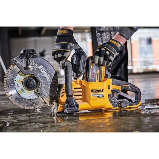 A person wearing DEWALT branded gloves operates a DEWALT cordless brushless power saw on a wet construction floor.
