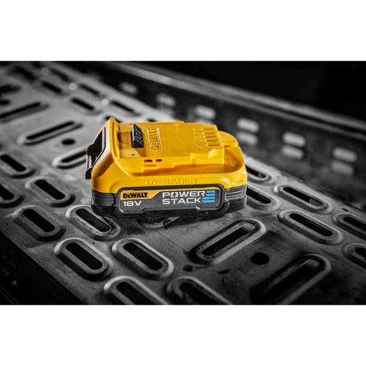 A DEWALT 18V POWERSTACK lithium-ion battery pack placed on a metallic industrial surface.