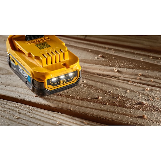 Close-up of a DEWALT DCBP034 18V POWERSTACK battery pack placed on a wooden surface with wood shavings scattered around.