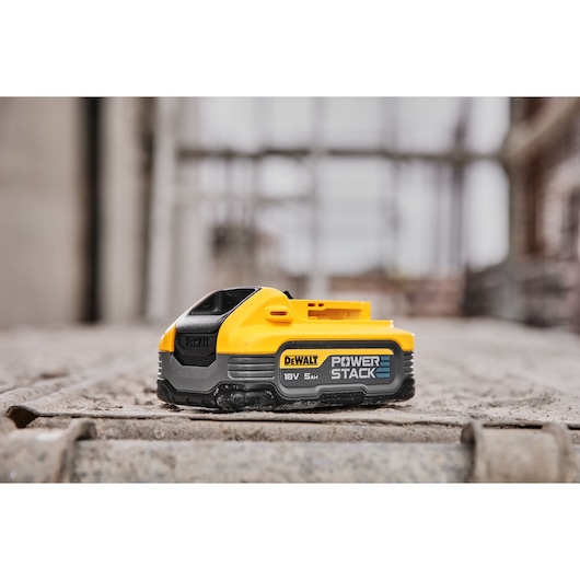 DEWALT POWERSTACK 18V 5Ah battery module placed on a rough concrete surface, photographed in a construction site setting.