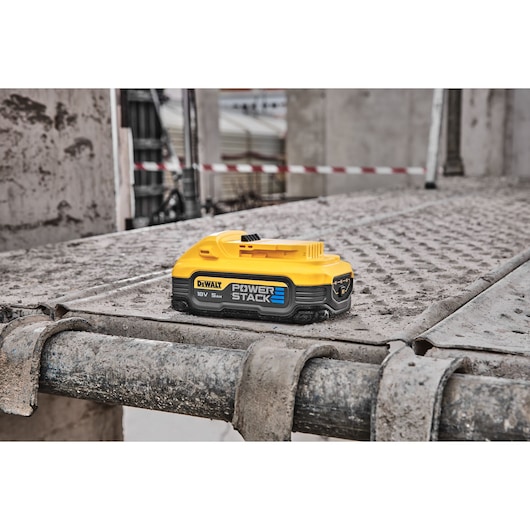 A DEWALT Power Stack 18V 5Ah battery is shown placed on a dirty, industrial metal surface at a construction site.