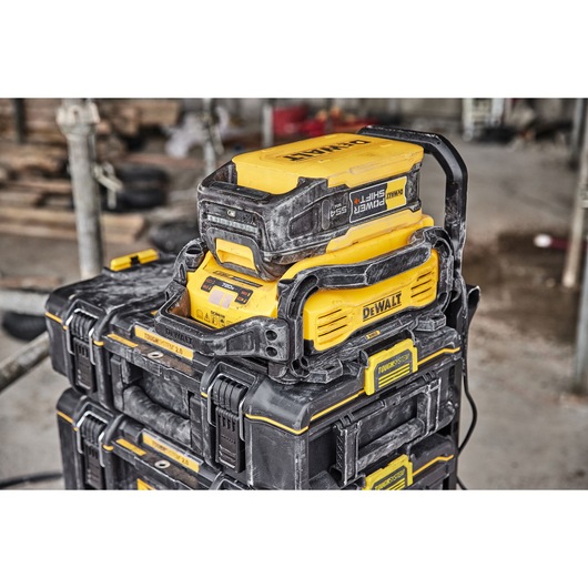A DEWALT PowerShift 54V battery charger and power station placed on top of a stack of DEWALT ToughSystem toolboxes in a dusty workshop environment.