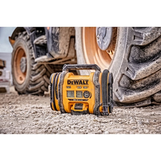 DEWALT DCC018N portable air compressor shown on a construction site, placed on gravel in front of large vehicle tires.