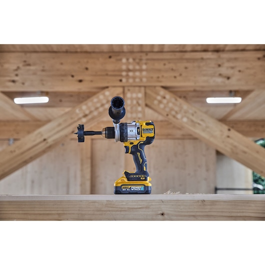 A DEWALT cordless drill with a drill bit attached, positioned on a wooden beam inside a structure with exposed wooden framing.