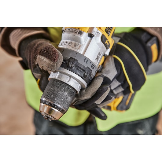 Close-up of a person wearing gloves and a safety vest, adjusting the settings on a yellow and black cordless drill.