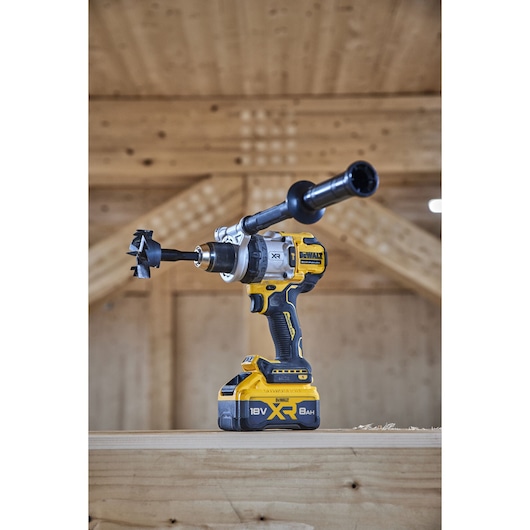 A DEWALT 18V XR cordless drill with an auger bit and side handle is placed on a wooden surface in a workshop setting.