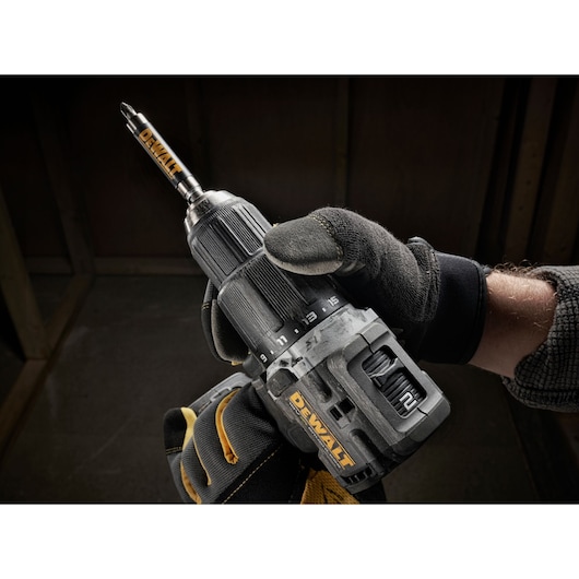 Close-up of a person wearing work gloves holding a DEWALT cordless drill with a DEWALT drill bit attached.