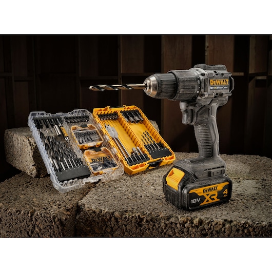DEWALT cordless drill with an 18V XR battery, positioned on concrete blocks. Next to it are two DEWALT drill bit sets in yellow and transparent cases, containing various drill bits and accessories.