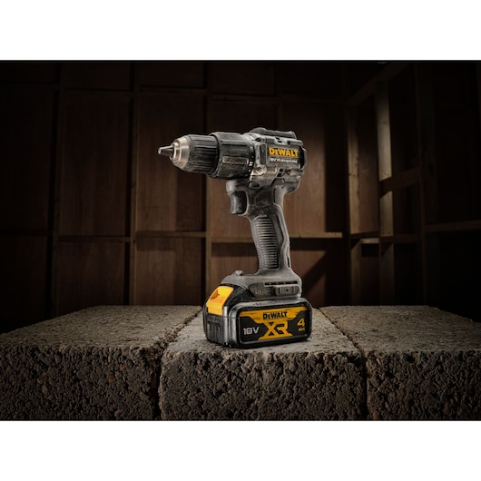 A DEWALT 18V XR cordless drill with a 4.0Ah battery is standing upright on a concrete block, with a wooden background behind it.