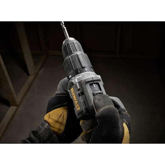 Close-up of a person wearing work gloves holding a DEWALT cordless drill with a drill bit attached, taken in a construction environment.