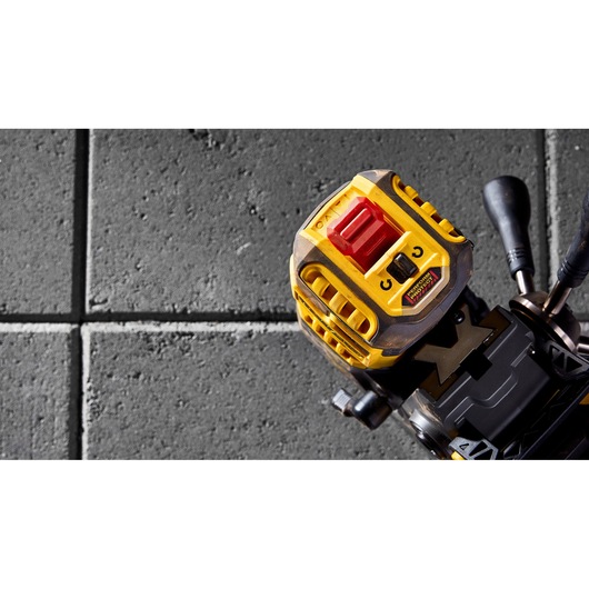 Close-up view of the DEWALT DCD1623N photography tool with a yellow and black design, featuring a red button, placed on a textured gray tile surface.