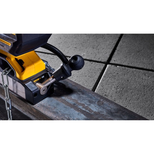 Close-up view of a DEWALT power tool, specifically the base and adjustment mechanism, positioned on a metal beam. Part of the yellow and black tool and a safety chain are visible.