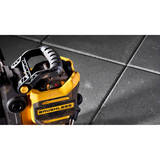 Close-up view of a yellow and black DEWALT brushless power tool with a textured grip handle. The tool is placed on a grey tiled surface.