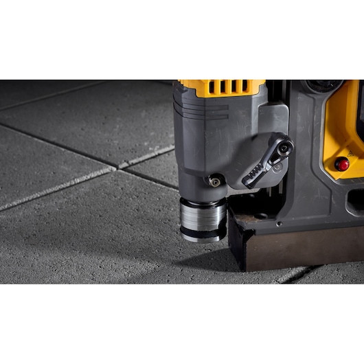 Close-up of a DEWALT power tool being used on a concrete surface. The image focuses on the tool's base and its drill attachment.