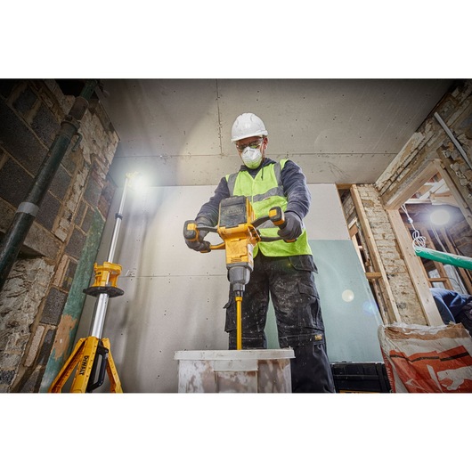 Worker mixes materials with a DEWALT tool indoors, wearing safety gear and a high-visibility vest.