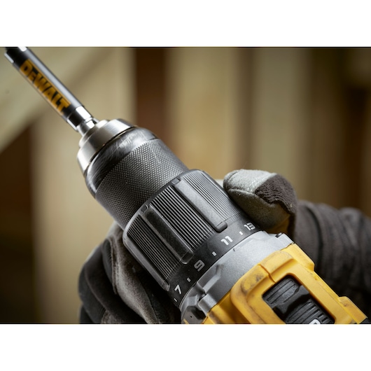 Close-up of a DEWALT cordless drill held by a gloved hand, focusing on the chuck and attachment.