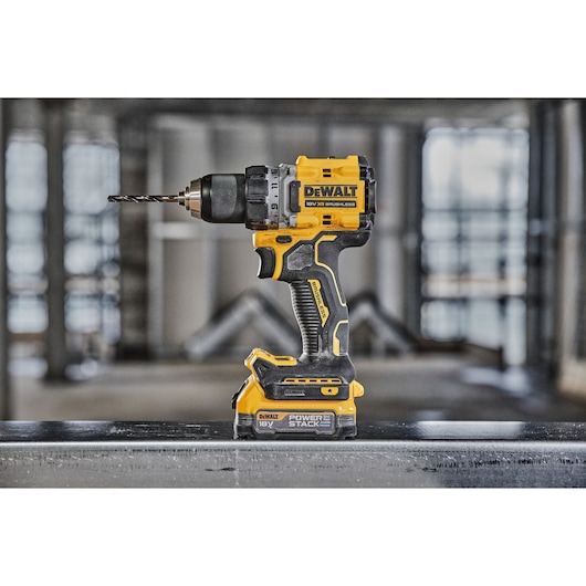 A DEWALT DCD800E1T 18V cordless brushless drill with POWERSTACK battery is shown standing upright on a metal surface in an industrial setting.