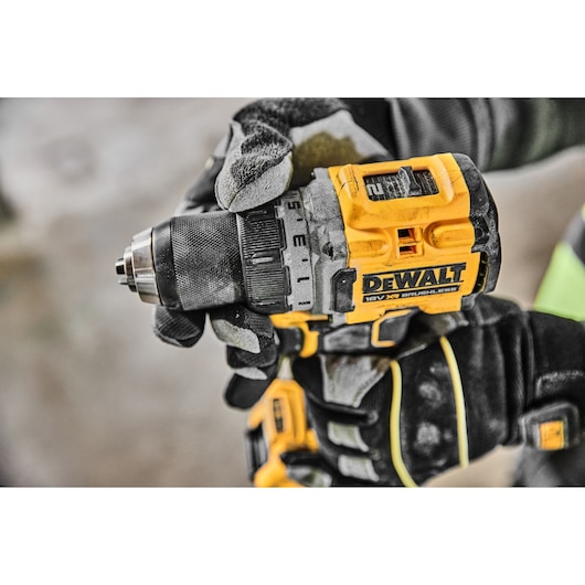 A close-up of a gloved hand holding a DEWALT 18V XR brushless cordless drill, showing the adjustable settings and branding.