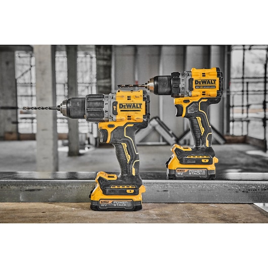 Two DEWALT cordless power drills with yellow and black design and POWERSTACK 18V battery packs, positioned on a metal beam in an industrial construction setting.