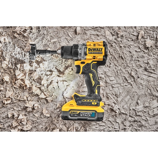 A DEWALT DCD800H2T cordless drill with a brushless motor and POWERSTACK battery is shown resting on a rough surface with wood shavings around it.