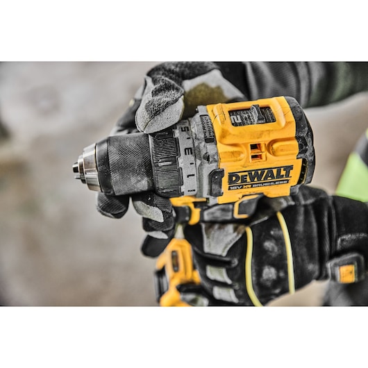 Close-up of a person wearing work gloves using a yellow DEWALT cordless drill.