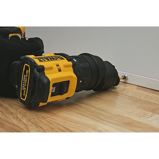 A DEWALT brushless cordless drill is shown driving a screw into a white panel on a wooden floor.