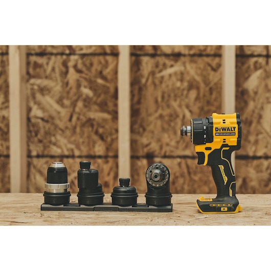 A DEWALT cordless drill with multiple interchangeable attachments displayed on a wooden workbench in front of a plywood wall.