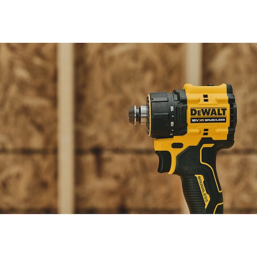 Close-up of a DEWALT 18V XR Brushless cordless drill with yellow and black casing, shown against a blurred wooden background.