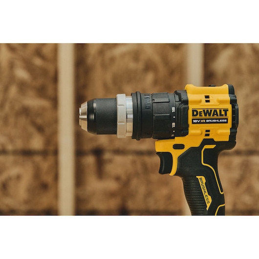 A close-up of a DEWALT 18V XR brushless cordless drill, shown against a blurred wooden background.