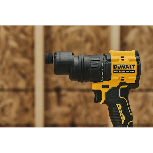 A close-up view of a DEWALT 18V XR brushless power drill, held horizontally with a blurred wooden background.
