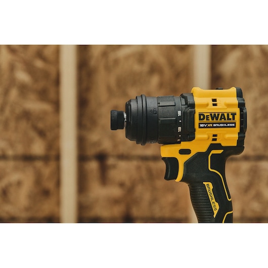 A close-up of a DEWALT 18V XR brushless cordless drill with a black and yellow design, shown against a workshop background with wooden panels.