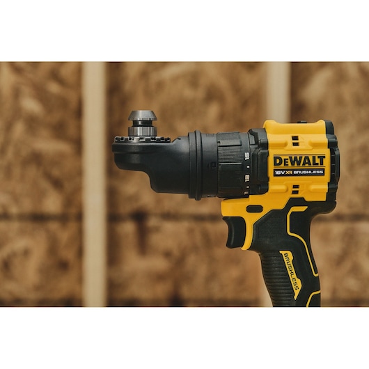Close-up of a DEWALT 18V XR brushless drill, showing the side view with its yellow and black casing, ergonomic grip, and drill chuck. The background is a blurred wood wall.