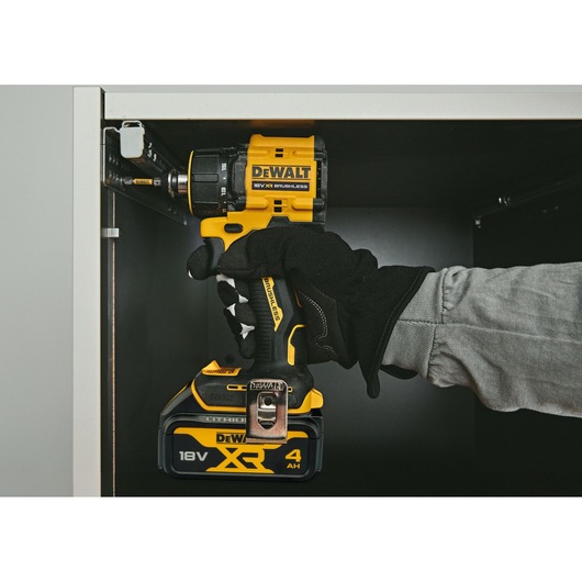 Gloved hand using a DEWALT 18V XR brushless drill inside a cabinet for assembly.