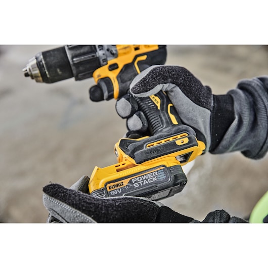 Close-up of a person wearing work gloves using a yellow and black DEWALT cordless power drill with a POWERSTACK 18V battery.