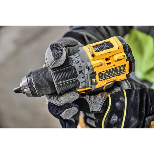 A close-up of a gloved hand holding a DEWALT 18V XR brushless cordless drill.