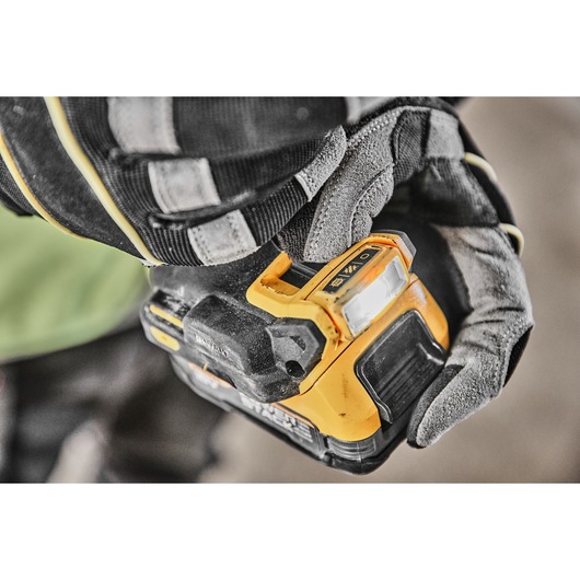 Close-up of a gloved hand holding a DEWALT cordless power drill with a visible LED work light and control switch.