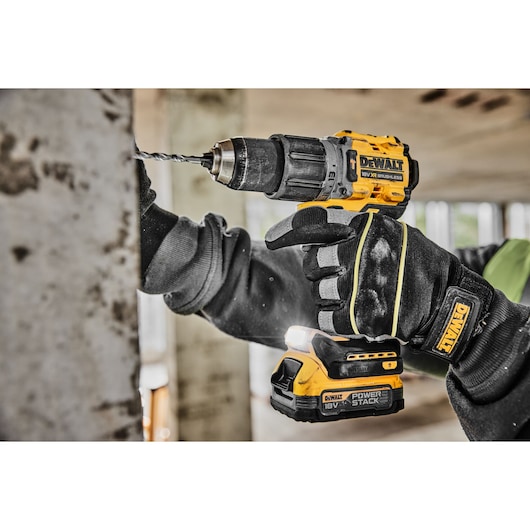 A person wearing protective gloves is using a DEWALT cordless power drill to drill into a metal surface in a construction setting.