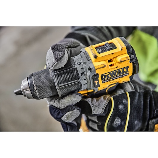 A close-up of a person wearing work gloves holding a yellow and black DEWALT 18V XR brushless cordless drill.