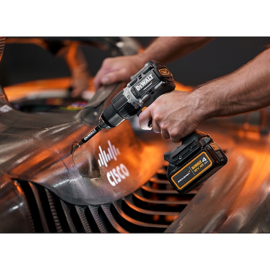 A person using a DEWALT cordless power drill to work on a carbon fiber surface near a Cisco logo.