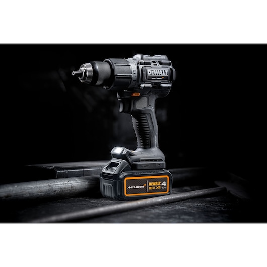 A DEWALT cordless drill with 18V XR battery, featuring McLaren branding, displayed on a dark industrial surface.