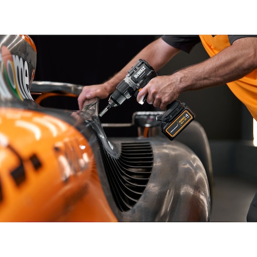 A person using a DEWALT cordless drill on a part of an orange and grey race car, focusing on a detailed close-up of the tool and the car surface.
