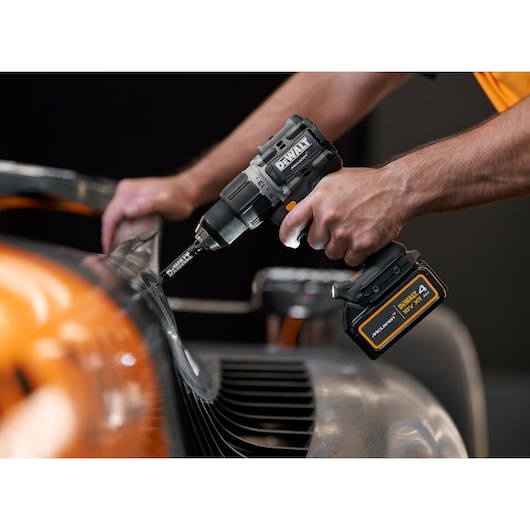 A close-up view of a person using a DEWALT cordless drill to work on a metal surface, with a DEWALT battery clearly visible. The scene suggests a professional or workshop environment.