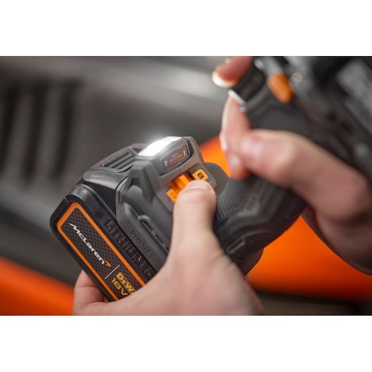 Close-up of hands operating a DEWALT 18V cordless power tool with McLaren branding, focusing on the LED light and control buttons.