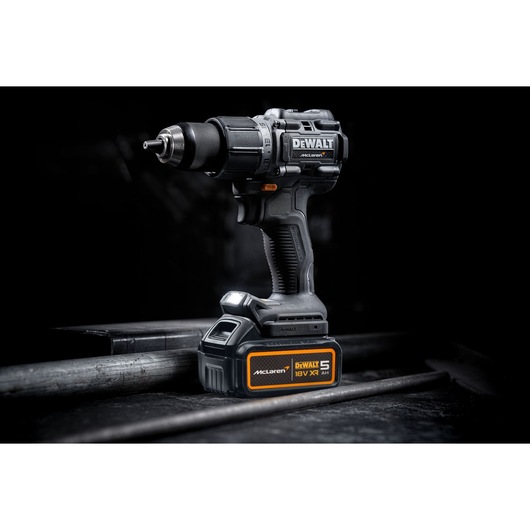 A DEWALT cordless power drill with 18V XR battery, featuring McLaren branding, standing upright on a dark industrial surface.