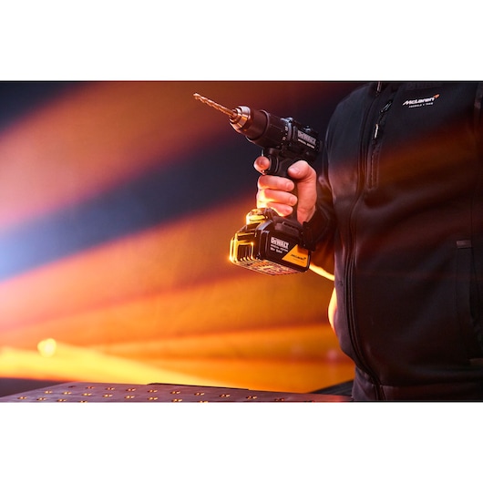 A hand holds the DEWALT x McLaren F1 Team 18V XR Special Edition Hammer Drill Driver with 5Ah battery