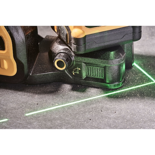 Close-up of a DEWALT laser level tool emitting bright green laser lines on a concrete surface, showing adjustment knobs and construction details.